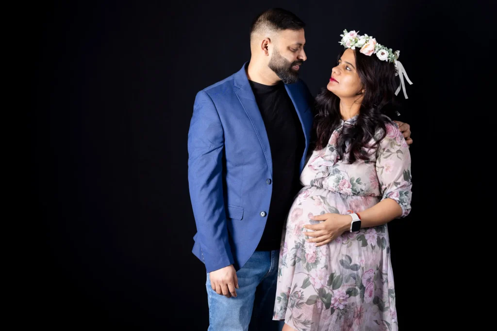 Expectant couple looking at each other, with the woman wearing a floral dress and flower crown.