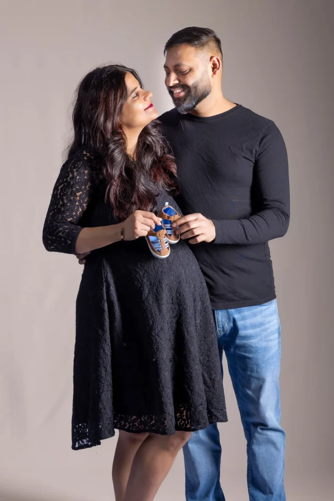 Expectant couple looking at each other while holding a pair of small baby shoes.