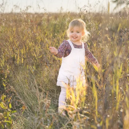 A toddler Girl walking in the tall grass full of smiles during a Beaudry Park Family Session by Winnipeg Family Photographer Jason Lee
