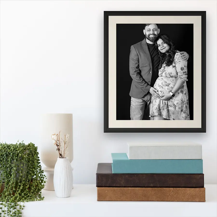 A stack of handcrafted linen and leather maternity photo albums and a museum-quality textured fine art print featuring an elegant maternity portrait