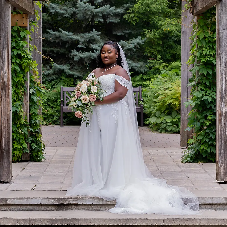 A bride in a white flowing gown posing among the statues and lush greenery at the Leo Mol Sculpture Garden in Assiniboine Park