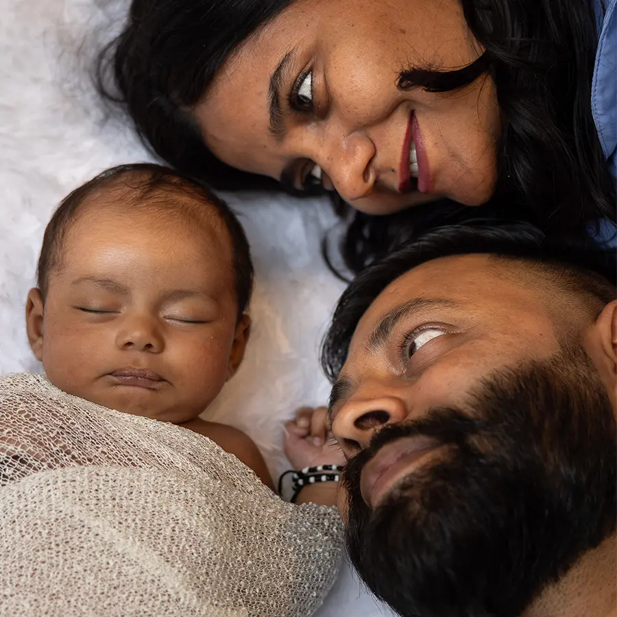A mother and father laying down with their heads close to their newborn baby, gazing at them during a Winnipeg studio session with Winnipeg Newborn Photographer Jason Lee.