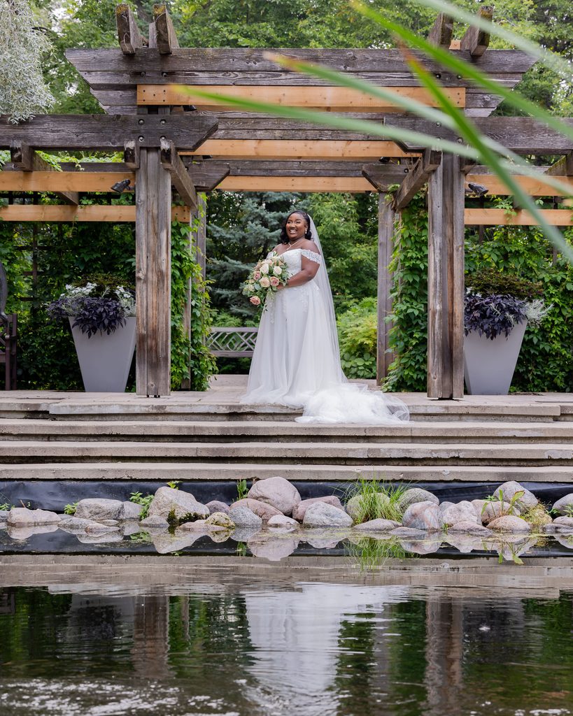 Bride posing beside the pond and pergola at Leo Mol Sculpture Garden