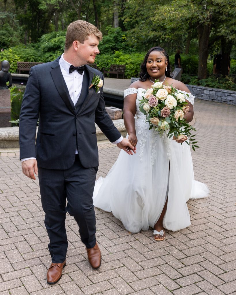 Newlyweds walking together through Leo Mol Sculpture Garden in Assiniboine Park