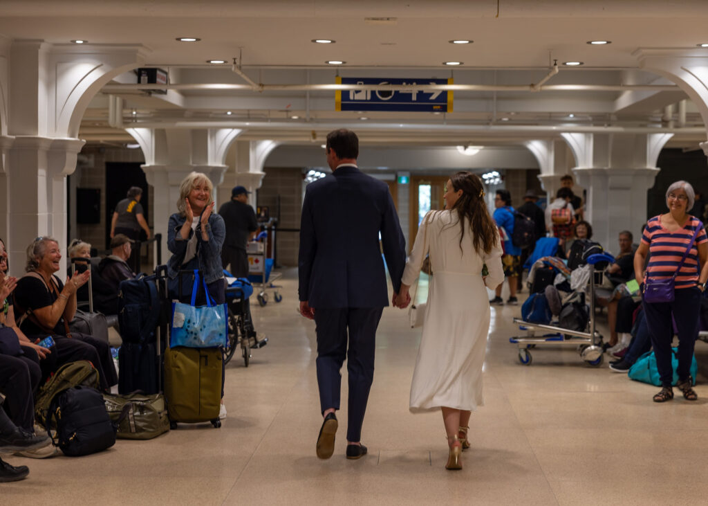 Newlyweds walking through Winnipeg's historic train station as waiting travellers applaud