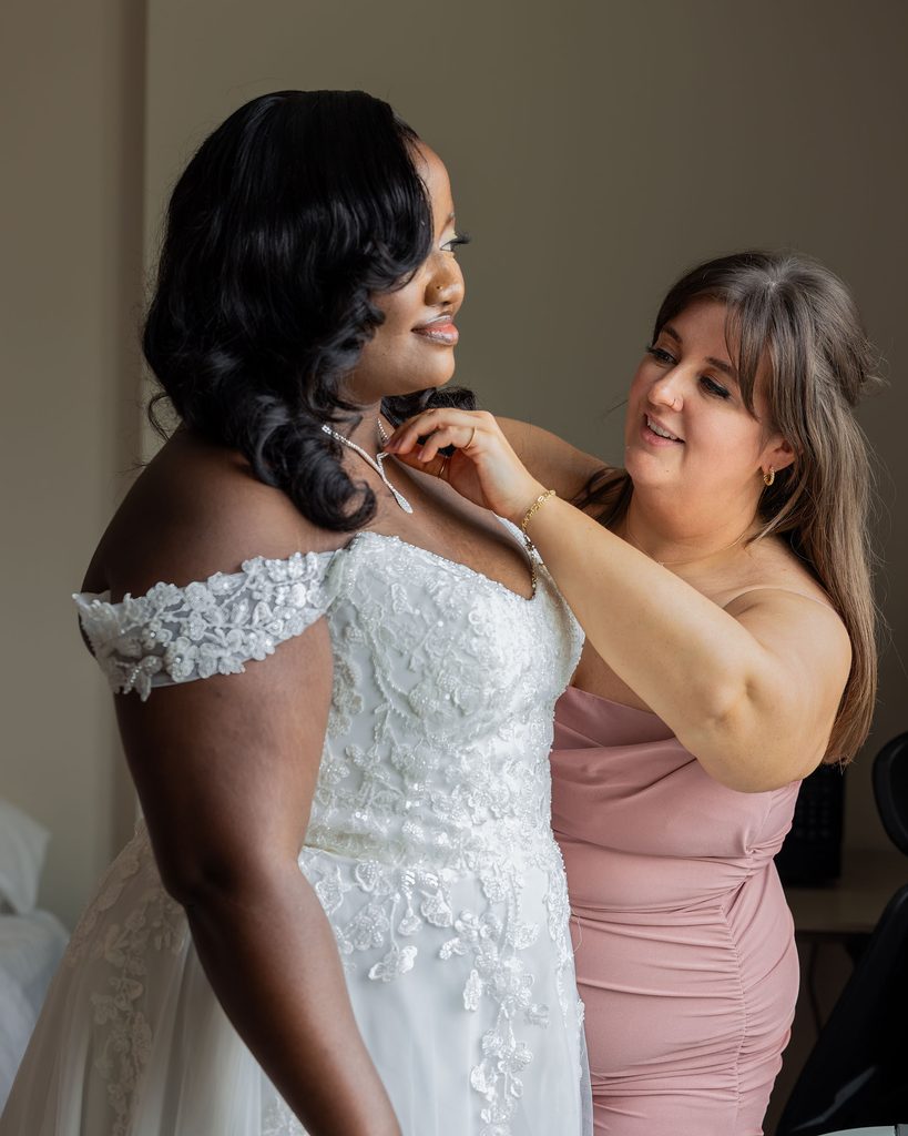 Bridesmaid helping the bride with her necklace before the ceremony