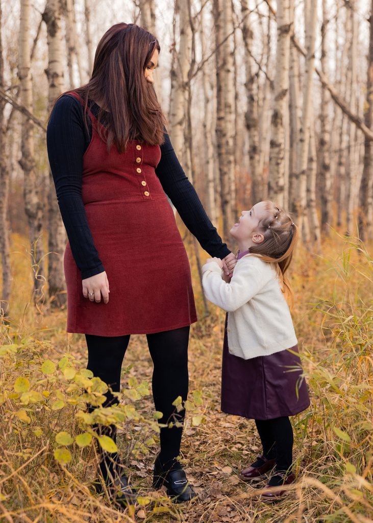 Mother embracing her daughter from behind during a playful fall family portrait