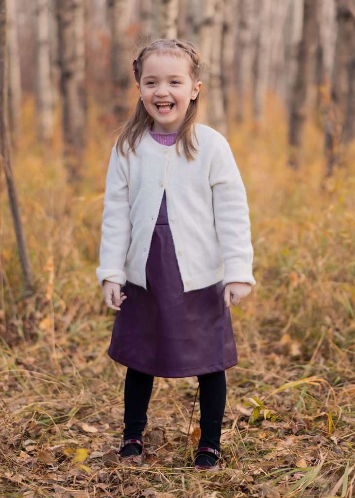 Young girl laughing during a fall portrait session among the trees in Assiniboine Forest