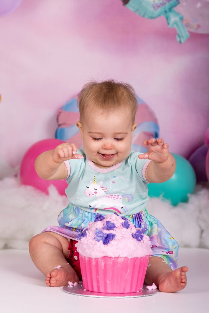 Baby reaching toward a pink cake during a first birthday cake smash