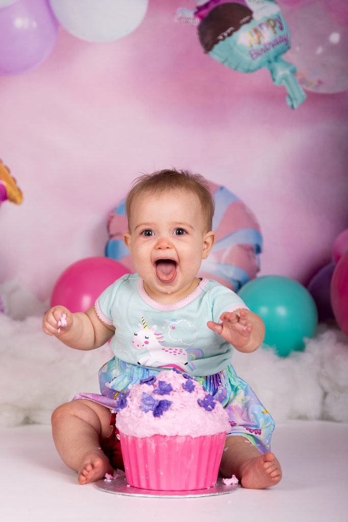 Baby laughing behind a pink cupcake cake during a first birthday session