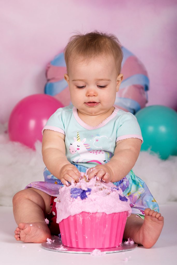 Baby pressing both hands into the icing on a pink birthday cake