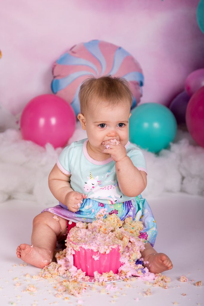 Baby tasting cake with frosting-covered hands during a cake smash