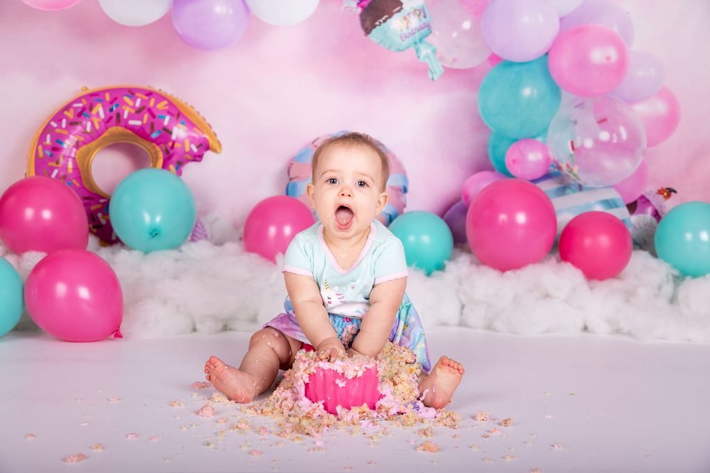 Baby smiling with a smashed cake and colourful balloons during a first birthday session