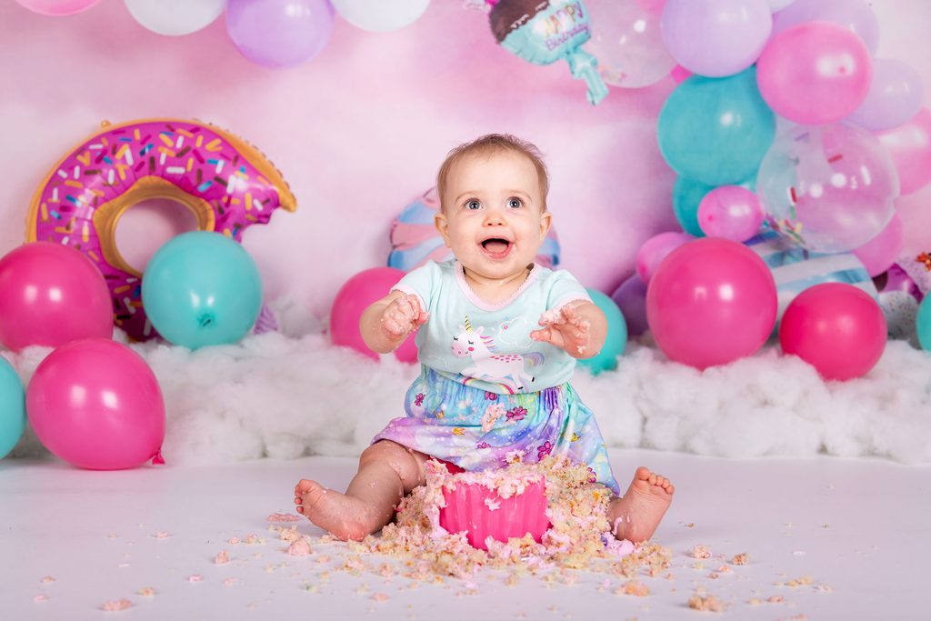 Baby smiling during a colourful first birthday cake smash session in Winnipeg