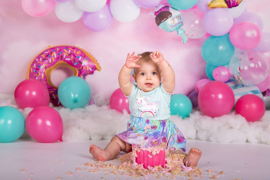 Baby raising icing-covered hands above a smashed birthday cake