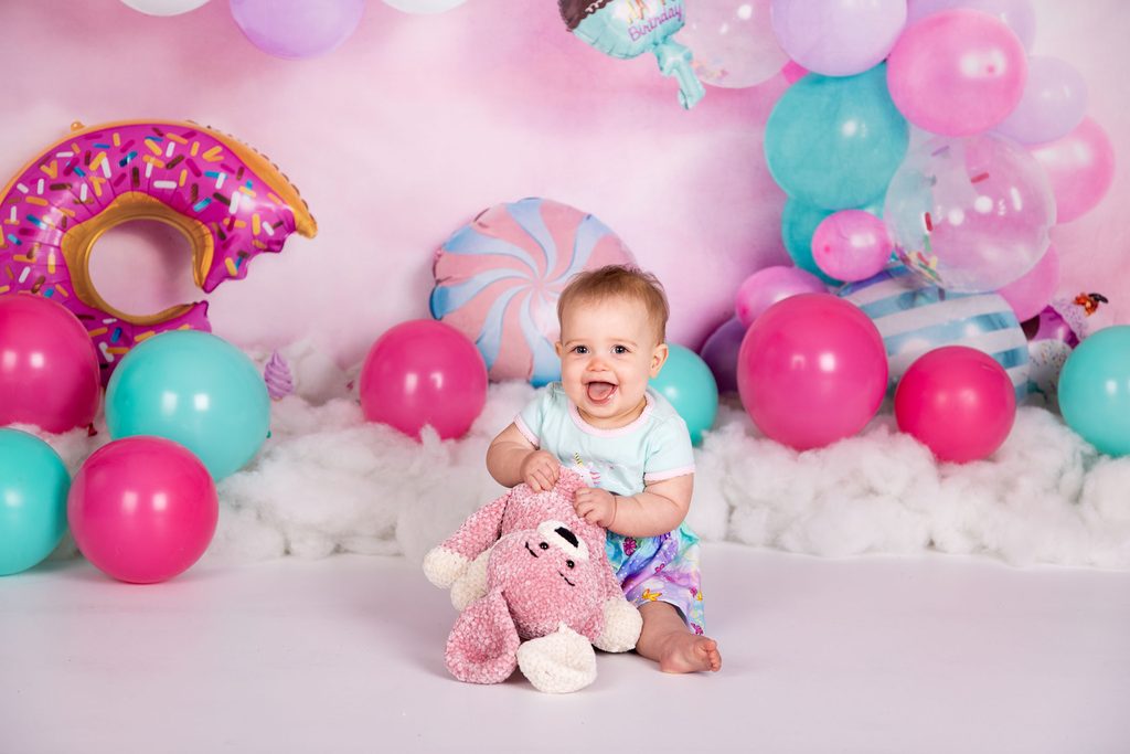 Baby smiling with a pink stuffed animal on a colourful first birthday portrait set