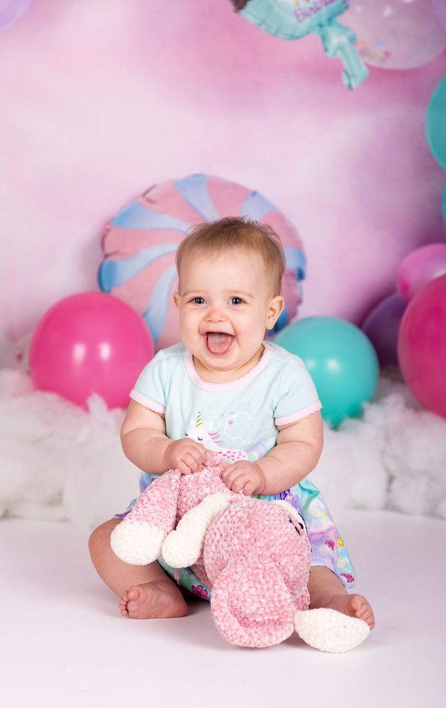 Smiling baby holding a pink stuffed animal during a studio first birthday session