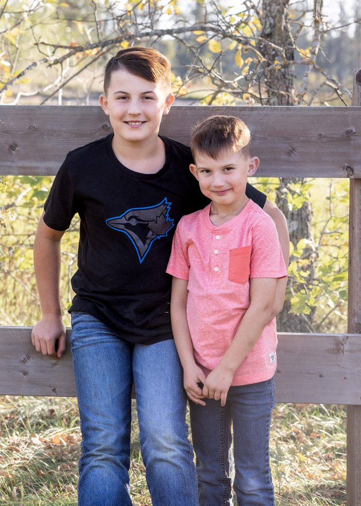 Two brothers smiling together beside a wooden fence during their fall family session