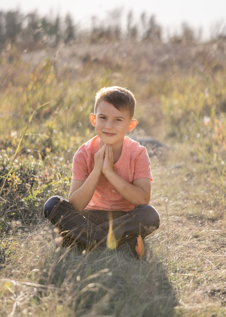 Young boy sitting cross-legged in the autumn grass at Alf Hole Goose Sanctuary in Whiteshell Provincial Park