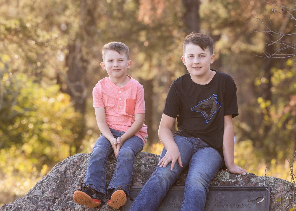Two brothers sitting together at the Alf Hole Goose Sanctuary sign in Whiteshell Provincial Park