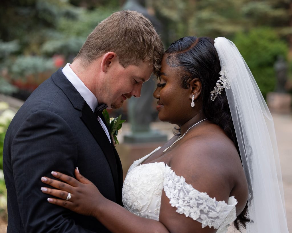 Bride and groom embracing with their foreheads touching in a garden.