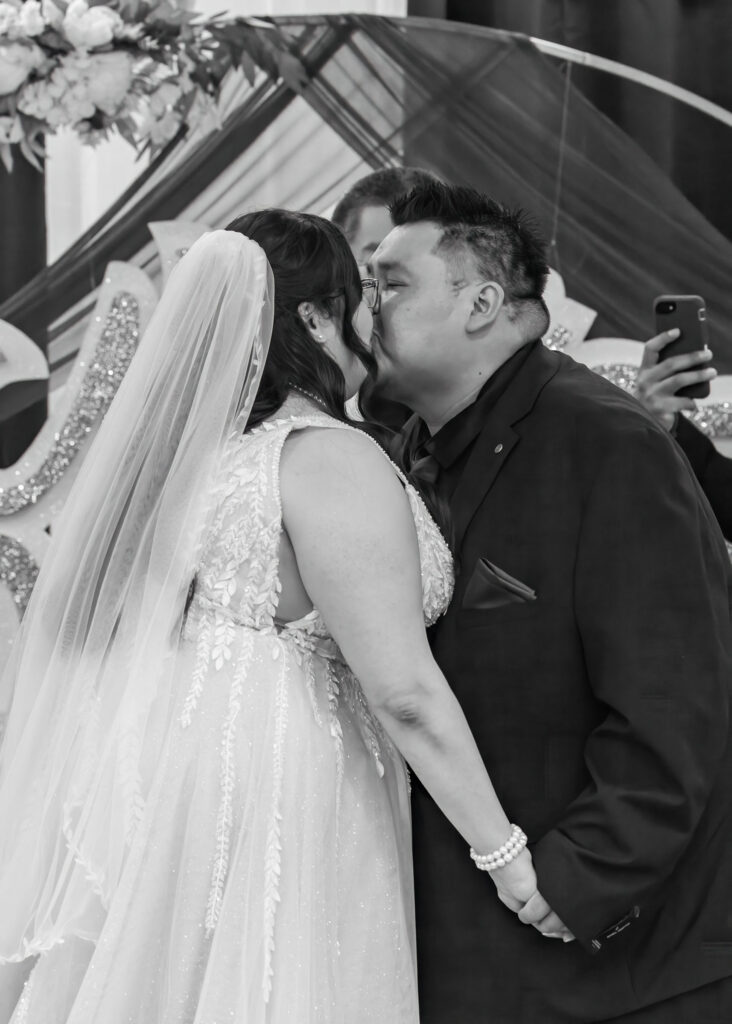 Bride and groom sharing their first kiss during an indoor Winnipeg wedding ceremony