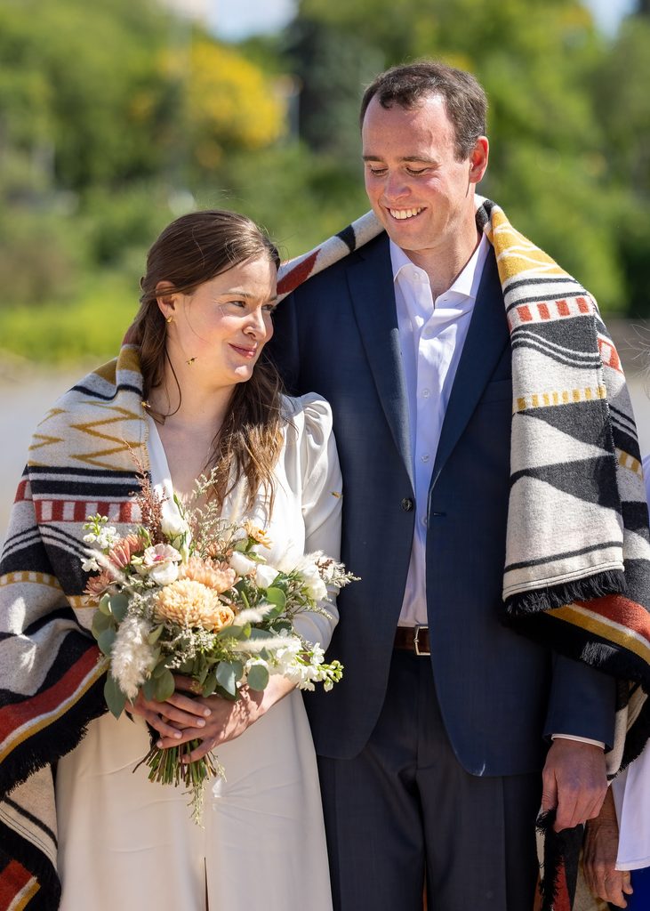 Bride and groom wrapped in a patterned blanket during their Métis wedding ceremony at The Forks in Winnipeg.