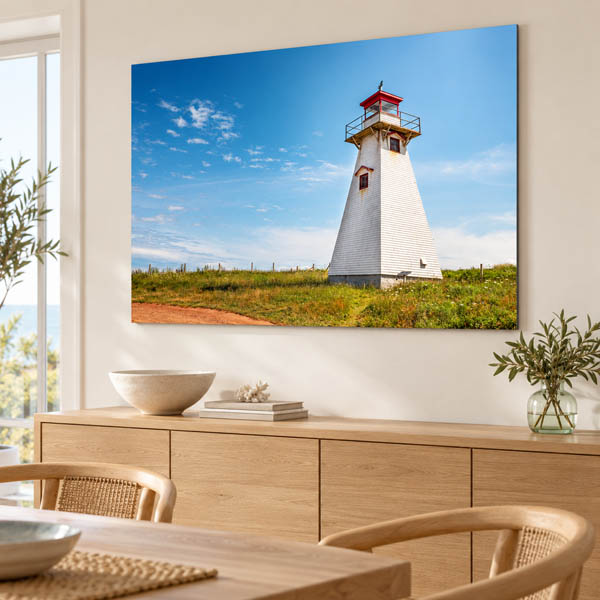 Print of Cape Tryon Lighthouse beneath a blue sky displayed above a wooden console in a bright room.