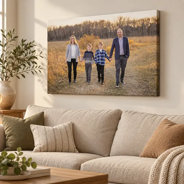 Canvas portrait of a family of four holding hands in an autumn field, displayed above a linen sofa.