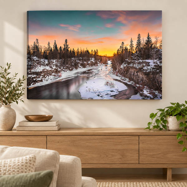 Canvas print of a snowy river beneath a colourful evening sky displayed above a wooden console.