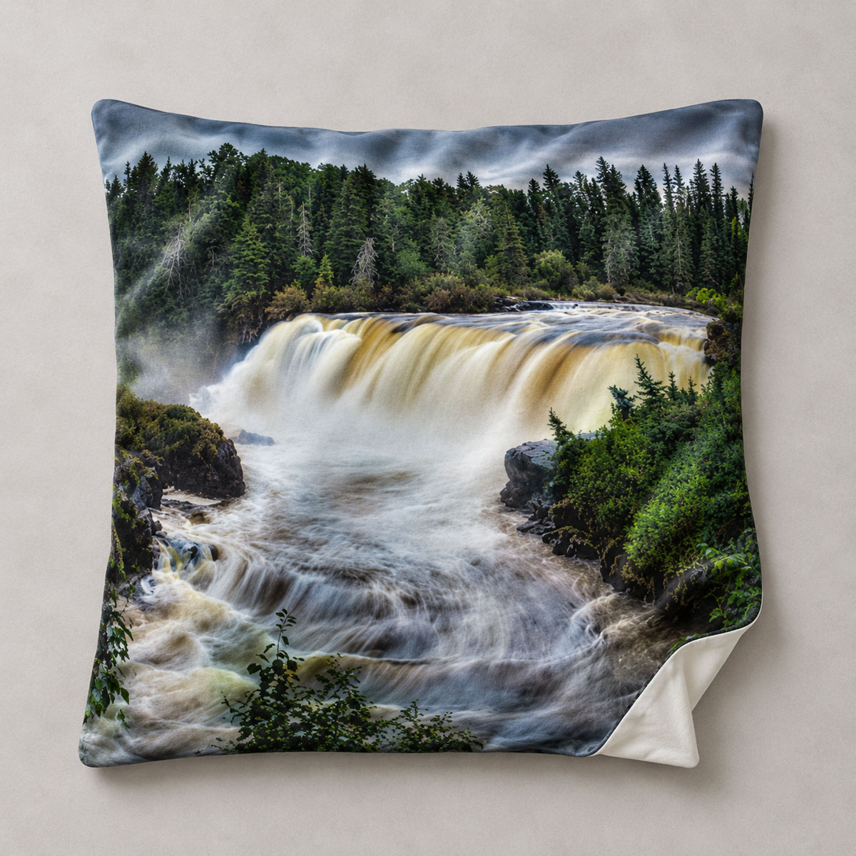 Square pillow cover featuring Pisew Falls cascading through evergreen forest, with one corner turned back to show the plain reverse.