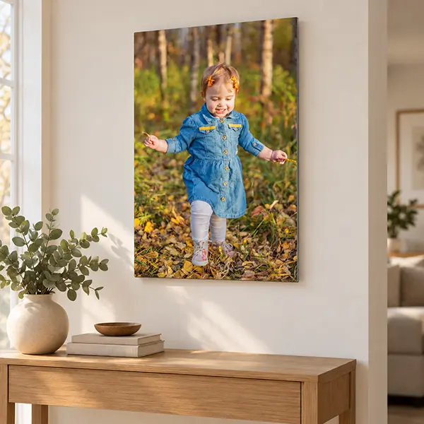 Metal print of a smiling toddler walking through autumn leaves, displayed above a wooden console.