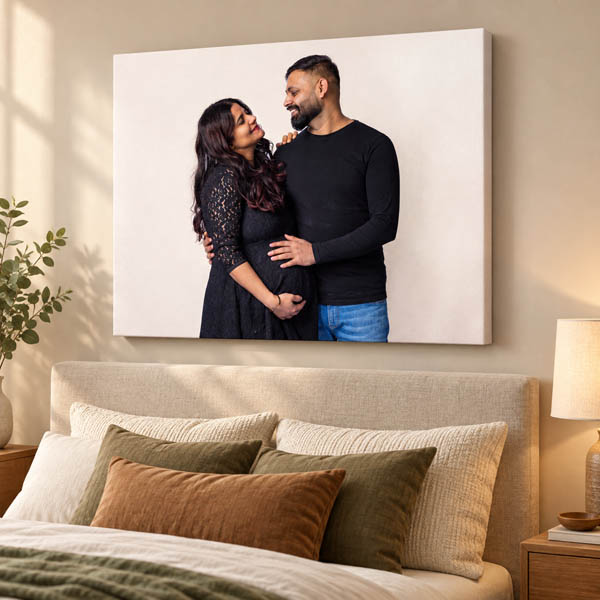 Canvas maternity portrait of a couple smiling at each other, displayed above a bed.