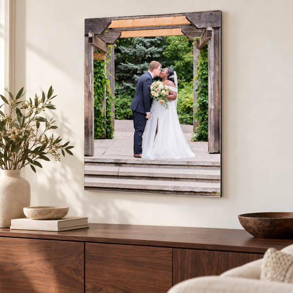 Wedding photo panel of a couple kissing beneath a wooden arch, displayed above a walnut sideboard.