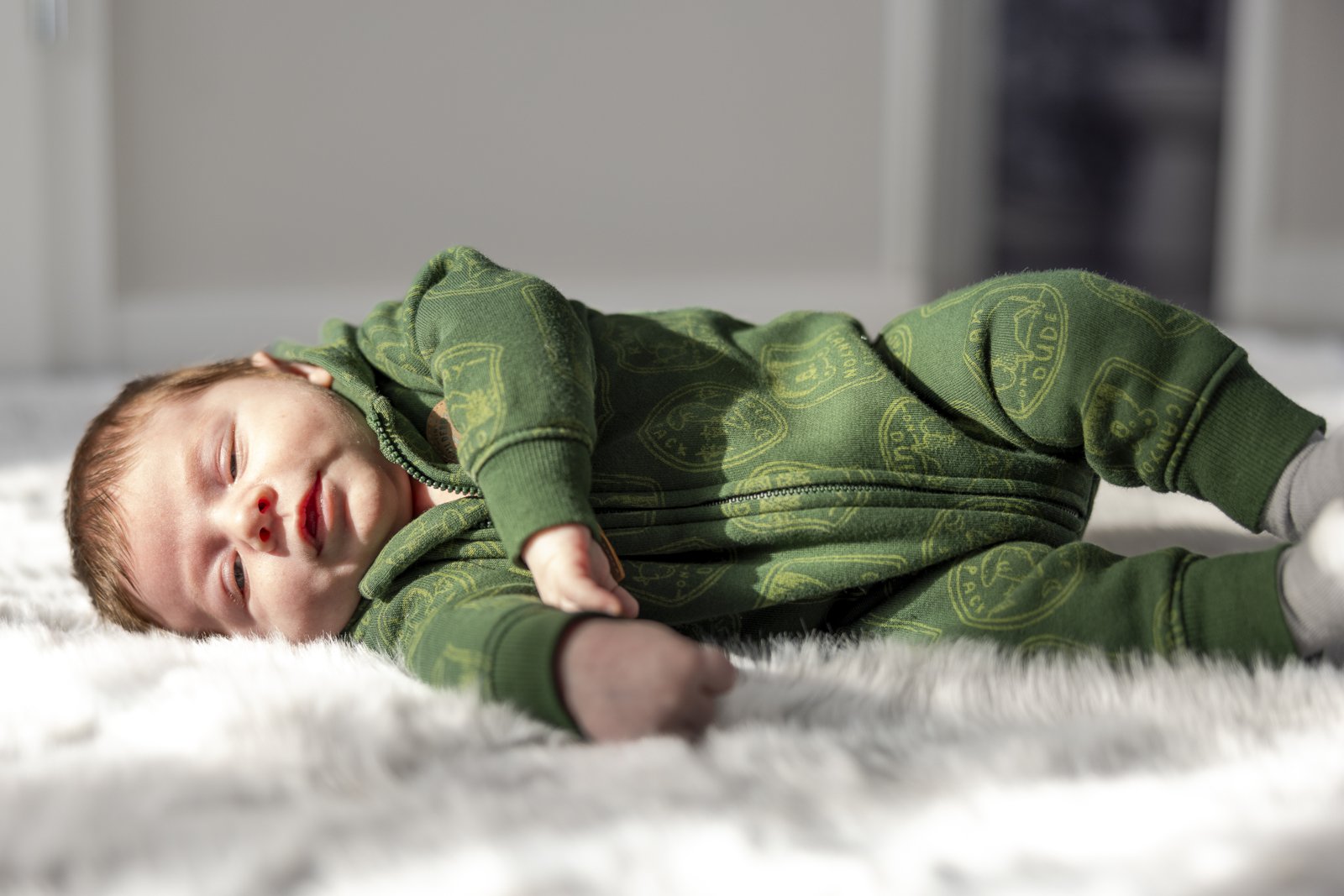 Newborn baby resting in a green outfit on a soft blanket at home.