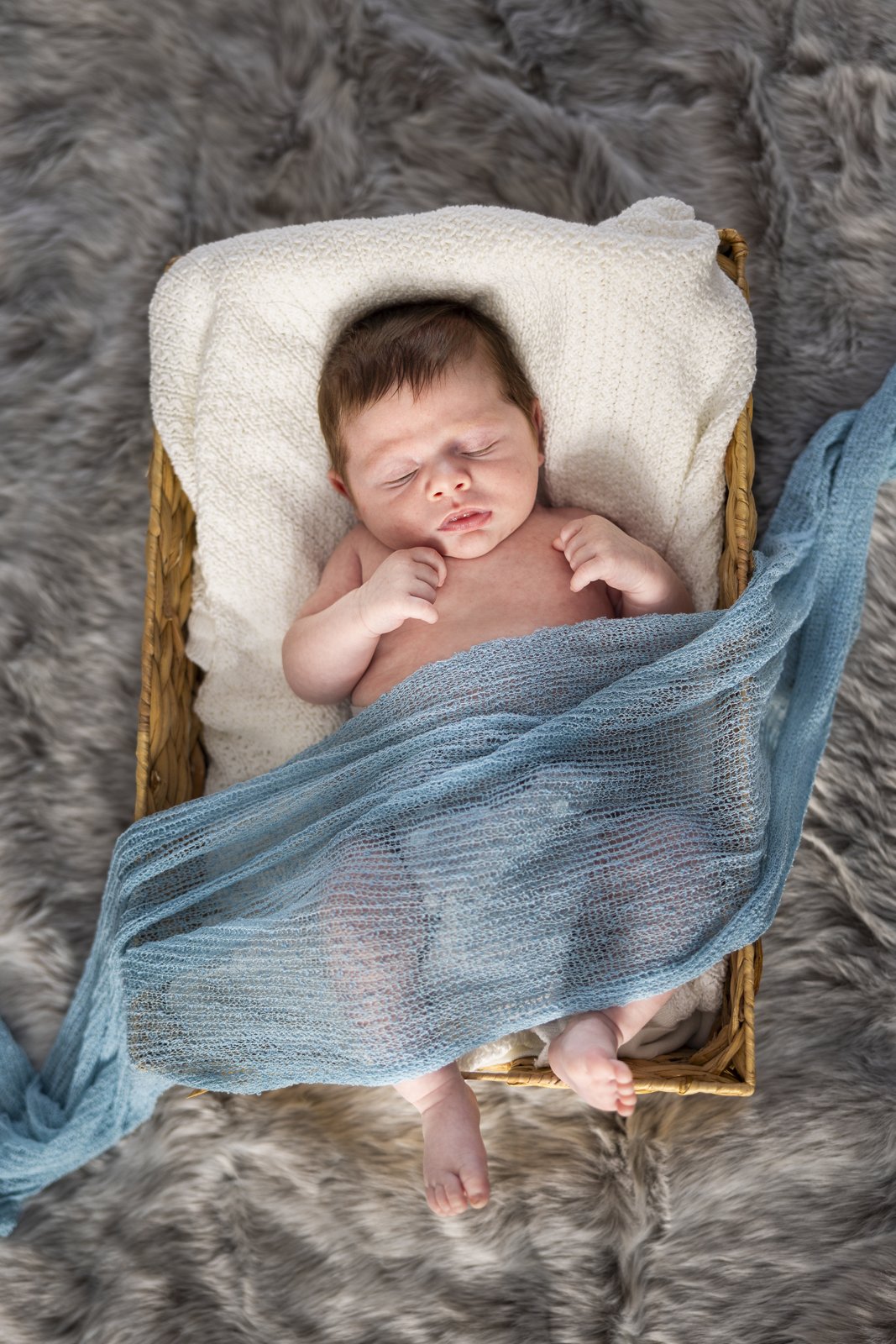 Newborn baby nestled beneath a blue blanket in a basket.