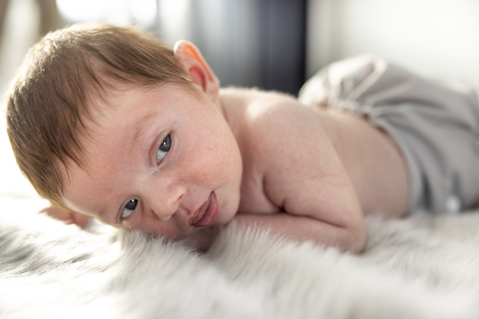 Awake newborn lying on a soft blanket during an in-home session.