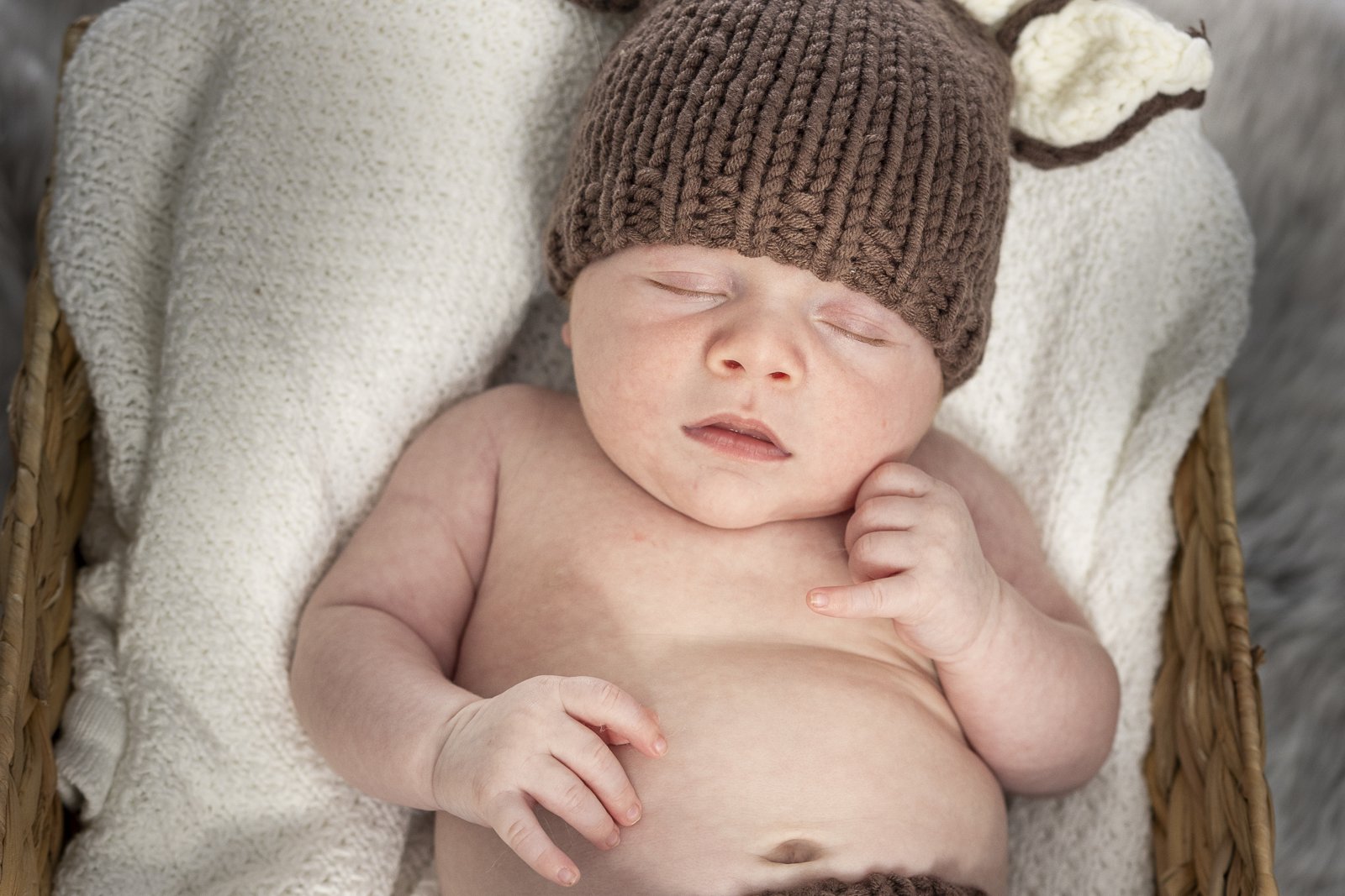 Newborn wearing a knitted bonnet while resting in a basket.