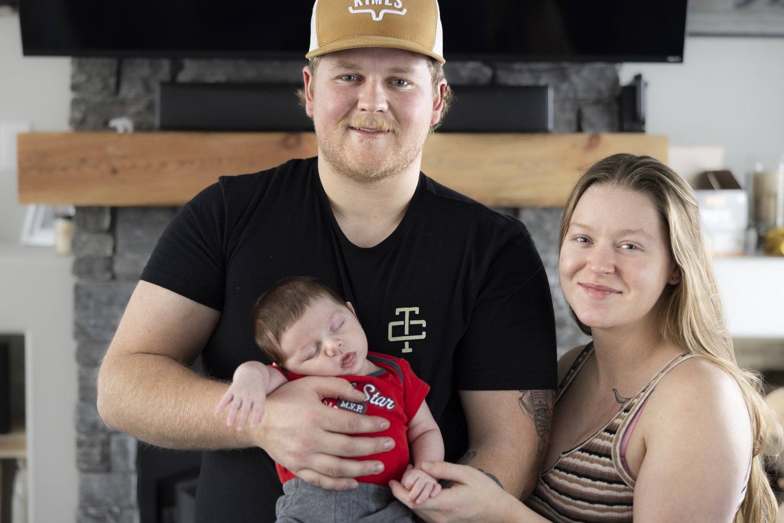 Both parents seated together holding their newborn baby at home.