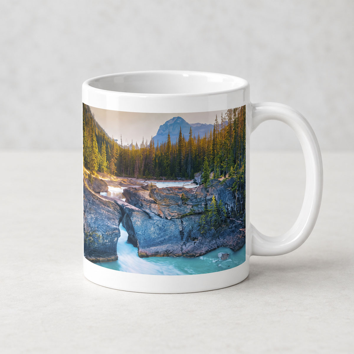 White ceramic photo mug featuring the rocky Natural Bridge, rushing water, evergreen trees and a mountain backdrop.