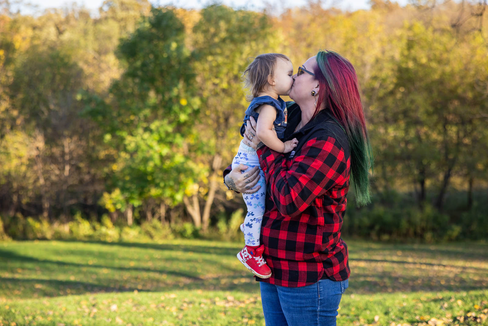Mother kissing her youngest child with soft autumn foliage behind them.