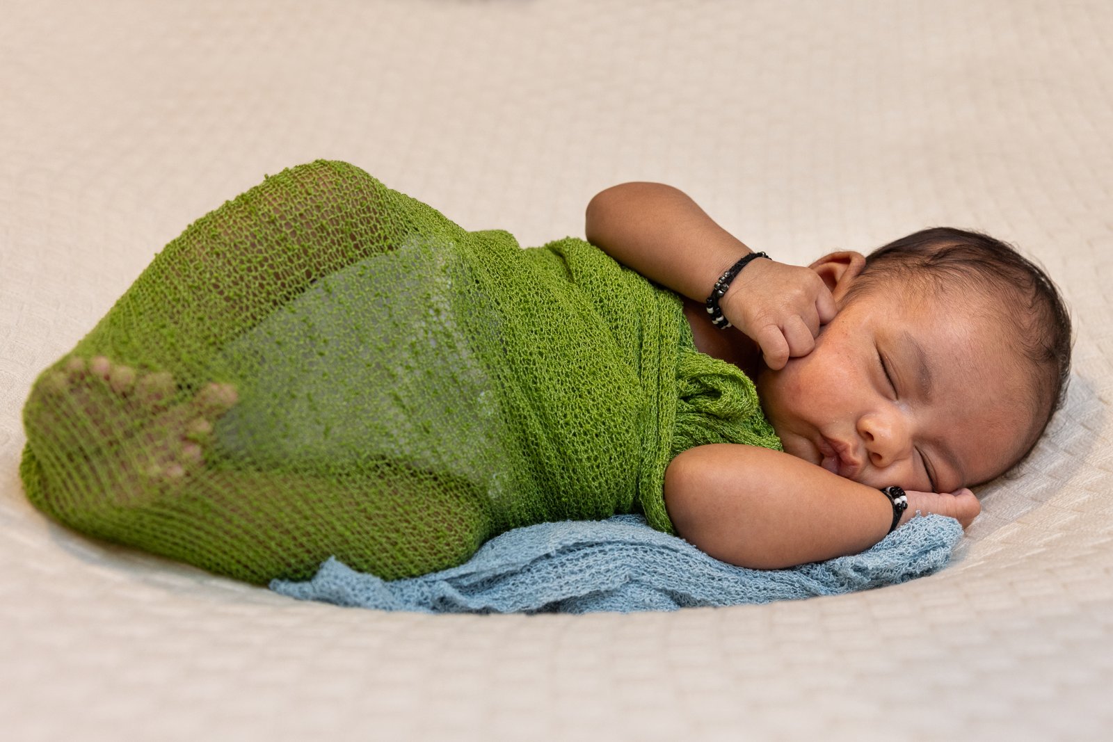 Sleeping newborn on a pale blanket in a green wrap.