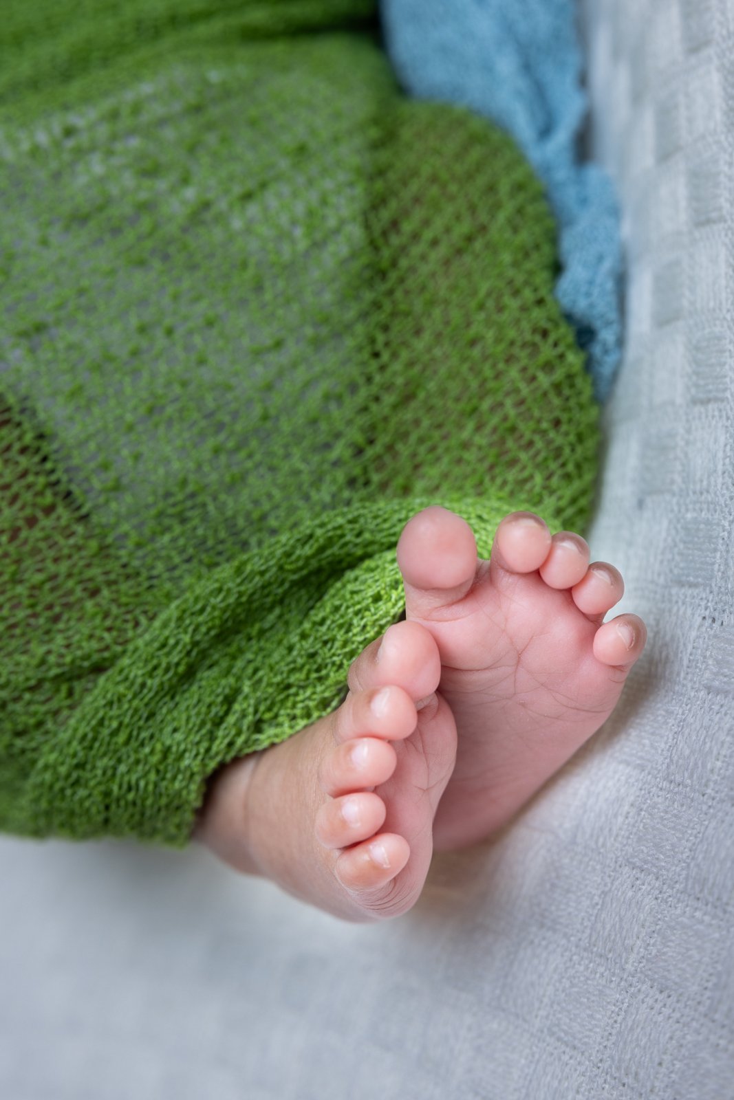 Close-up of tiny newborn feet beneath a green wrap.