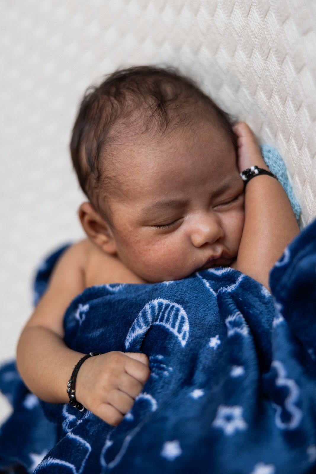 Sleeping newborn beneath a blue blanket patterned with moons and stars.