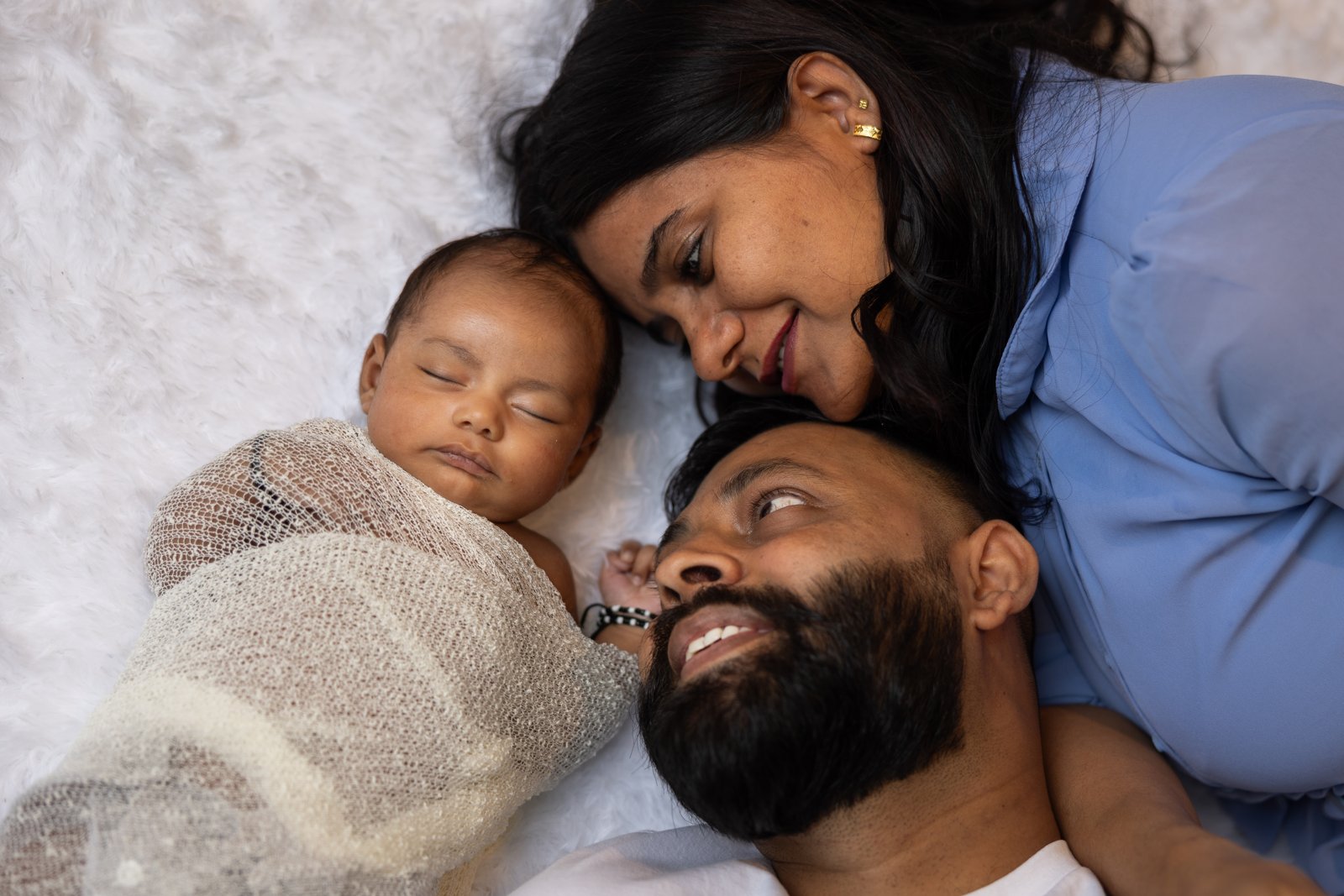 Both parents lying beside their sleeping newborn baby.