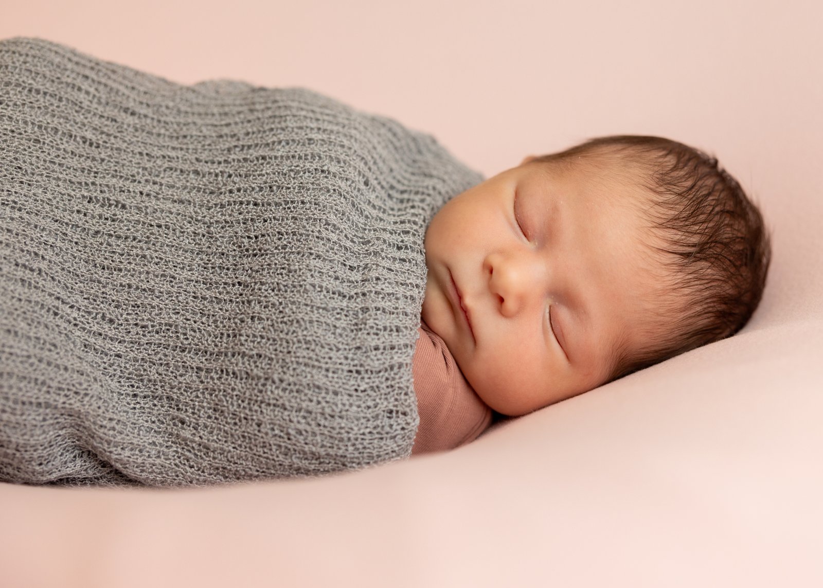 Newborn resting in a grey knitted wrap during a studio session.