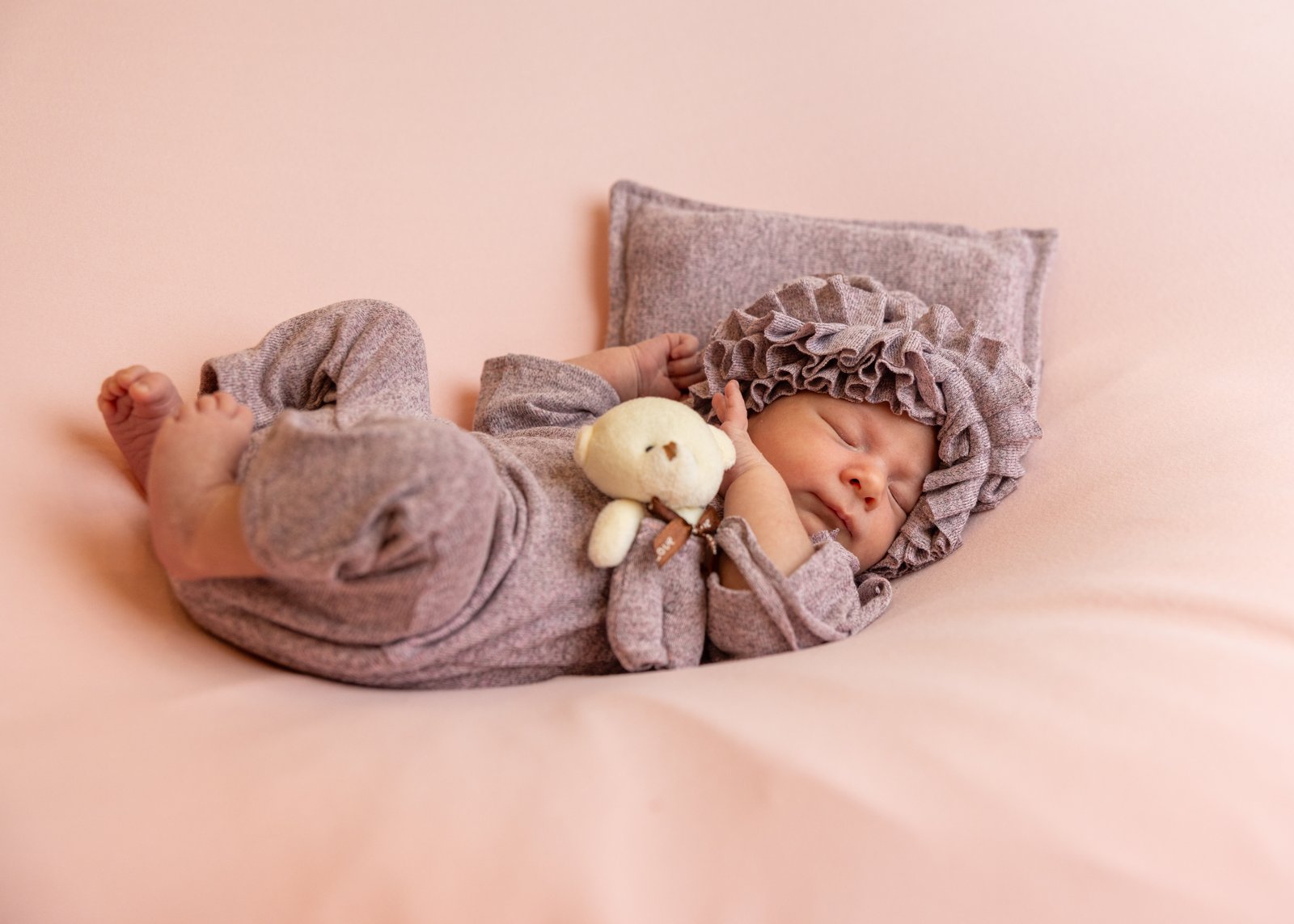 Newborn in a knitted bonnet beside a small soft toy.
